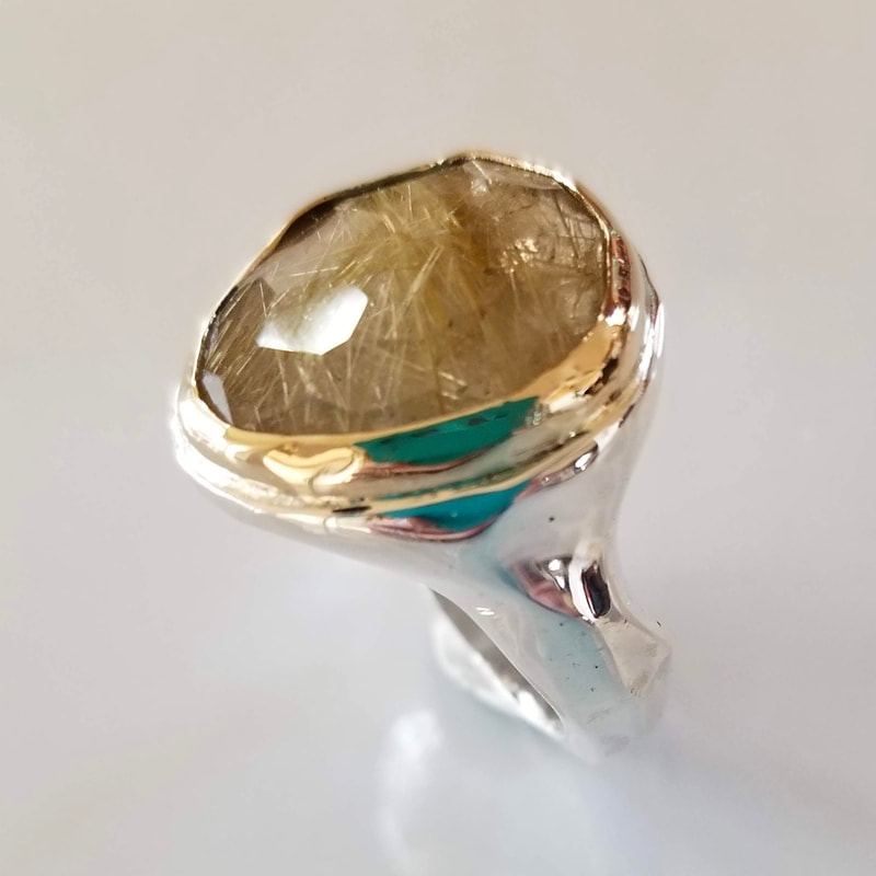 Gold and silver Ring with a large oval shaped Rutilated Quartz in the center.