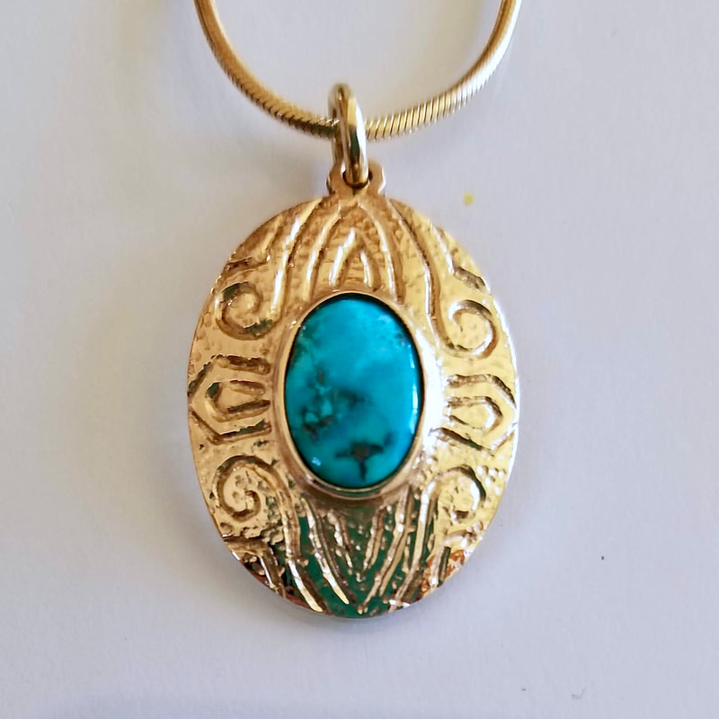 Patterned gold pendant with an oval Turquoise in the center.