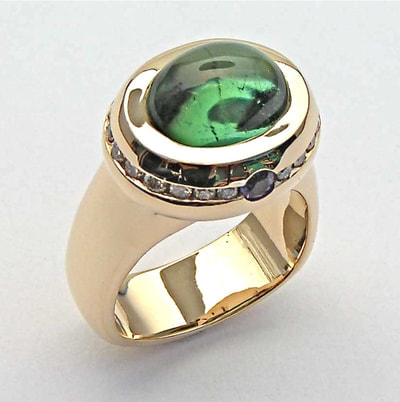14 Karat Yellow Gold ring with an oval Green Tourmaline and diamonds around the profile of the gold around this stone.