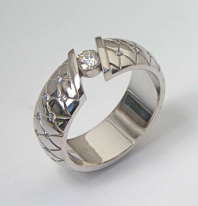14 Karat White Gold ring with one tension - set round Diamond and flush set spaced Diamonds down each side of the band.