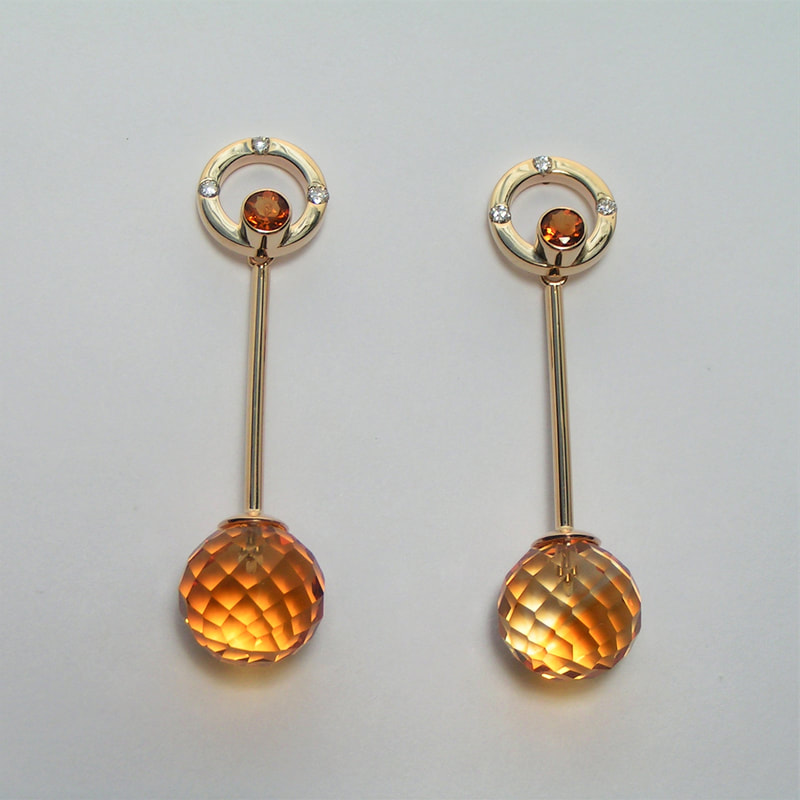 14 Karat Yellow Gold post earrings with a gold circle that has diamonds spaced around it, a small citrine in the center and a faceted Briolette Citrine at the bottom.