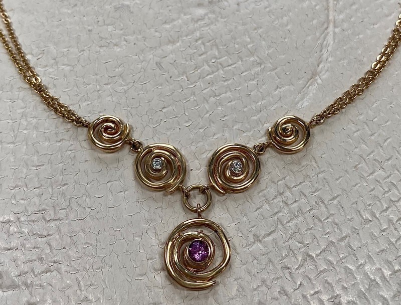 14 Karat Yellow Gold necklace with spiral shaped designs with one Pink Sapphire and diamonds with a double chain.