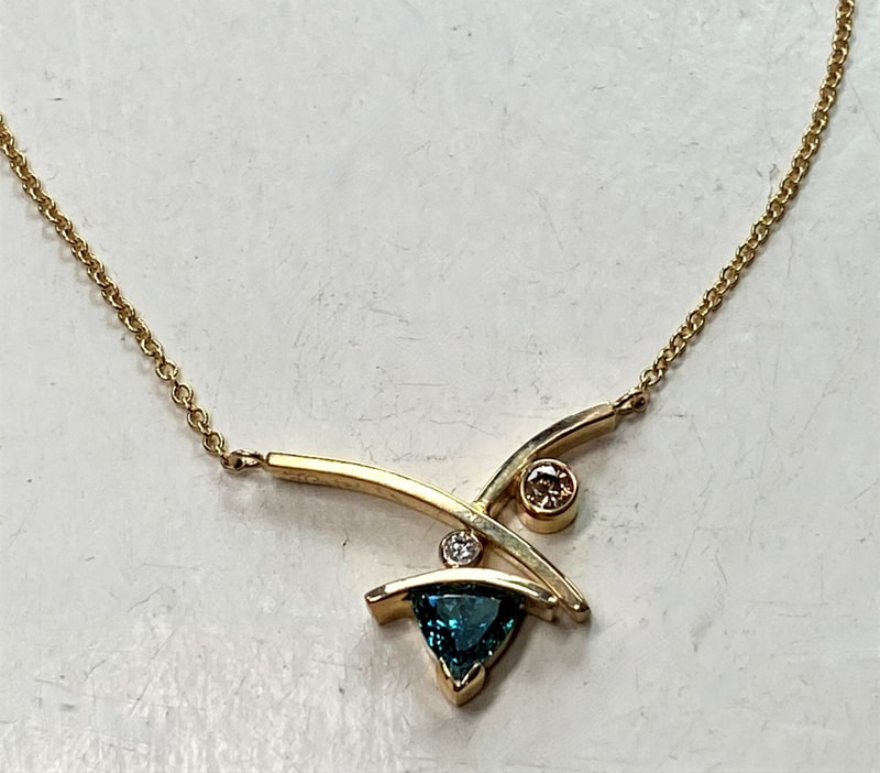 14 Karat Yellow Gold necklace with one trillion shaped Green Diamond, a bezel set Champagne Diamond and one small white diamond.
