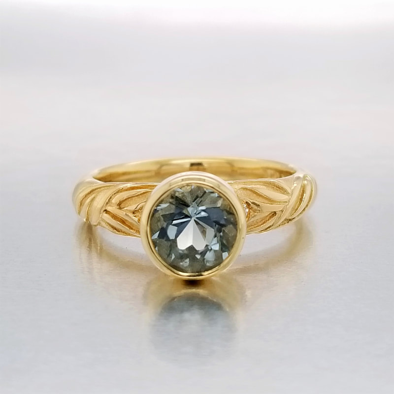 18 Karat Yellow Gold ring with one round  bezel set Aquamarine in the center and a sculpted leaf band.