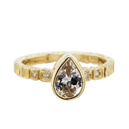 18 Karat Yellow Gold bezel set pear shaped White Sapphire in the center and flush set diamonds on the band.