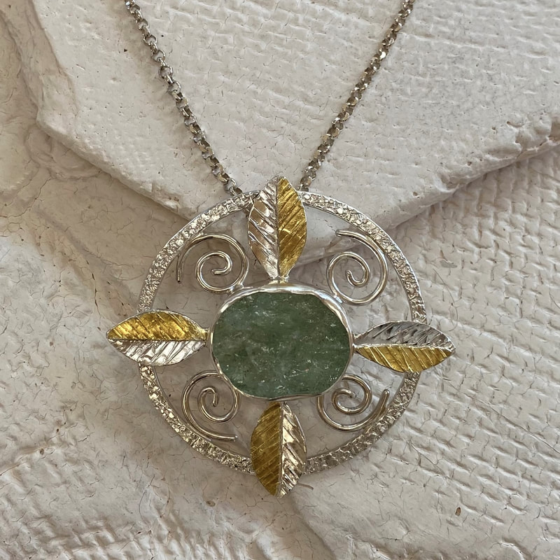 Silver and 22 Karat Yellow Gold open circle pendant with leaf designs and natural face aquamarine in the center.