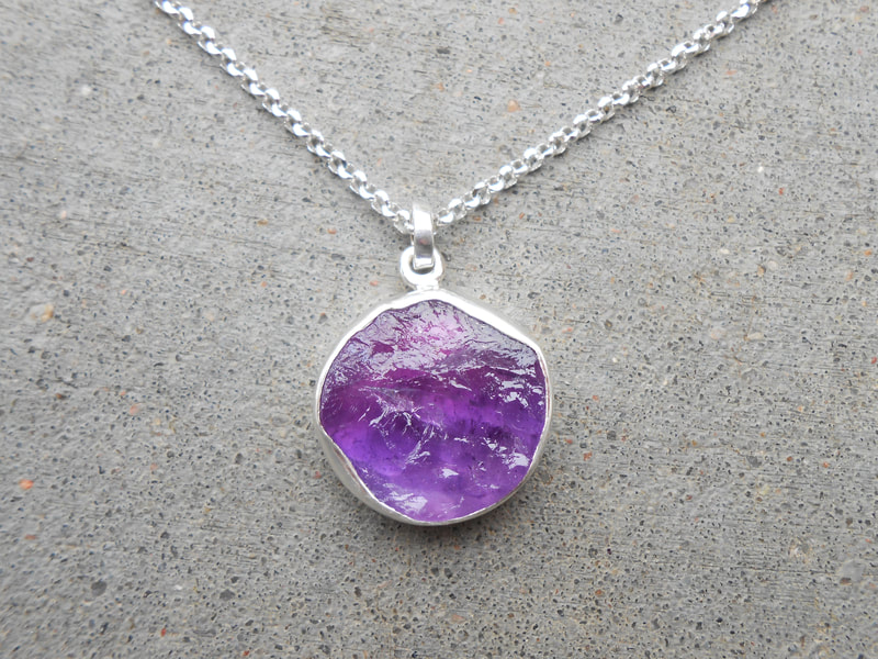 Silver bezeled natural face roughly round amethyst pendant.