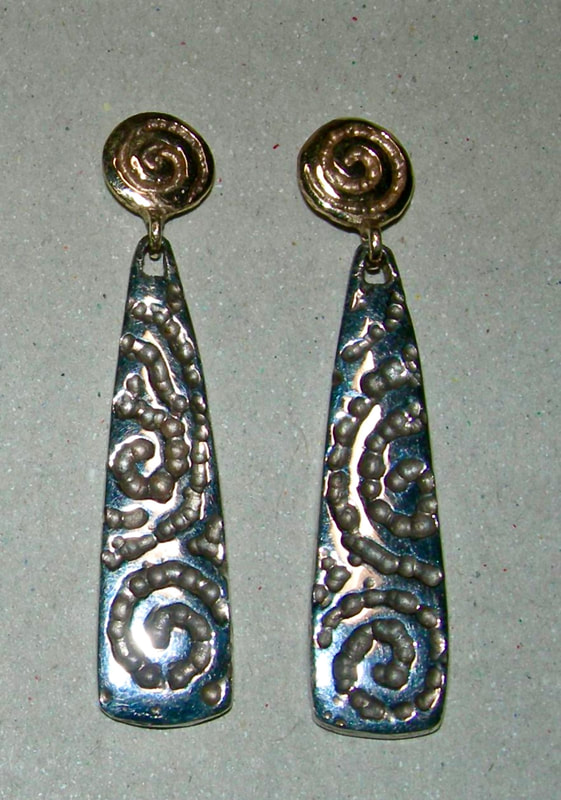 Carved dangle earrings with gold round tops and an elongated silver patterned dangle.