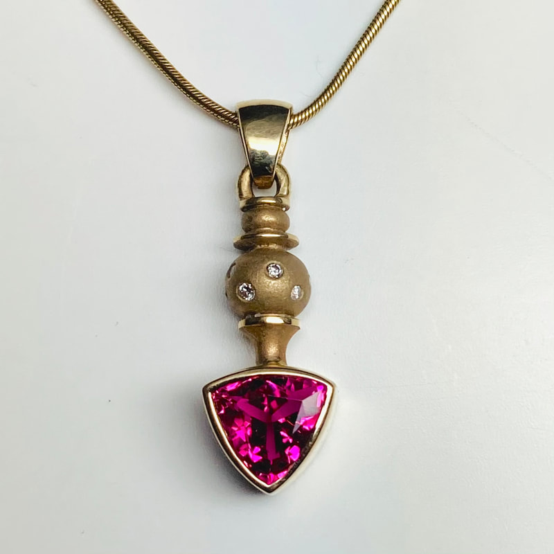 18 Karat Yellow Gold Pendant with a Trillion Pink Tourmaline and scattered diamonds.
