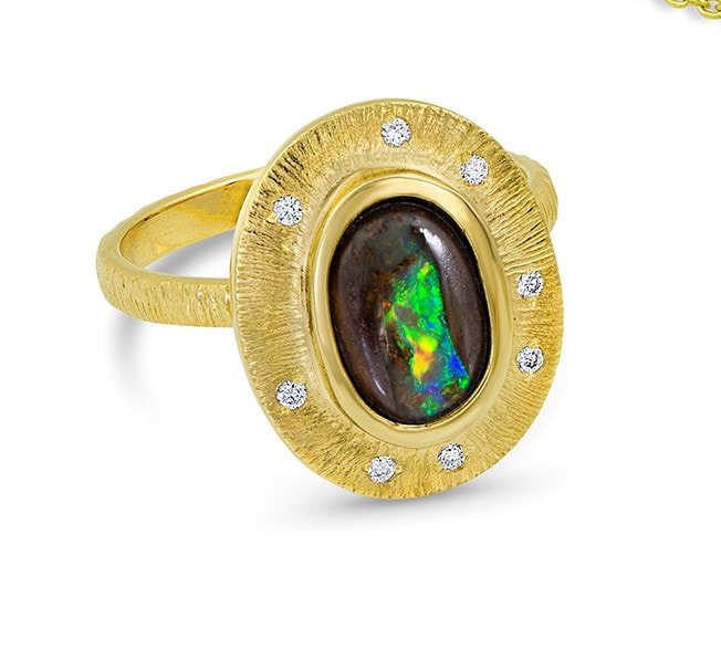 A gold ring with a natural oval black opal with a border around it having spaced inset diamonds and a textured band.