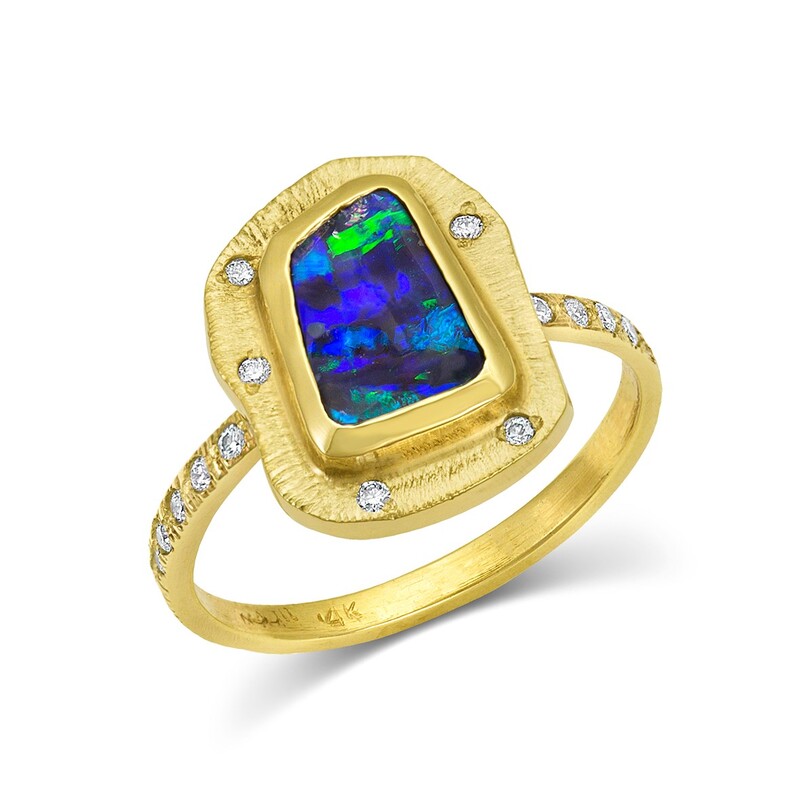 A gold ring with a natural elongated opal with a border around it having spaced inset diamonds and a textured band.