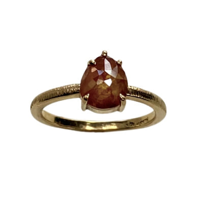 Yellow gold ring with one orange-ish pear shaped diamond in a four prong setting and a thin textured band.