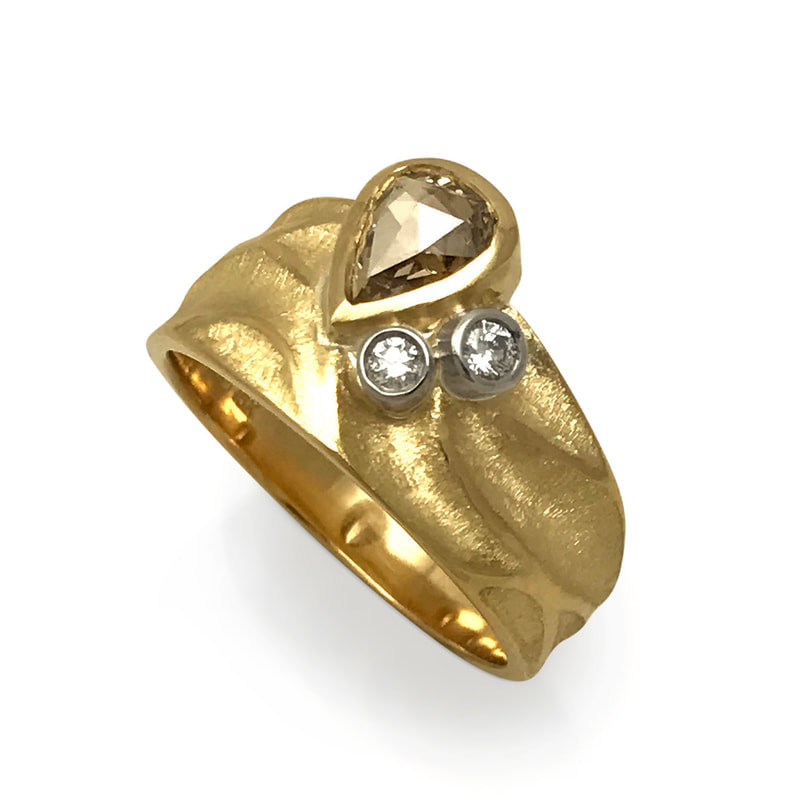 Gold ring with an off-set natural brown pear shaped diamond on one side and two small round diamonds accenting it.