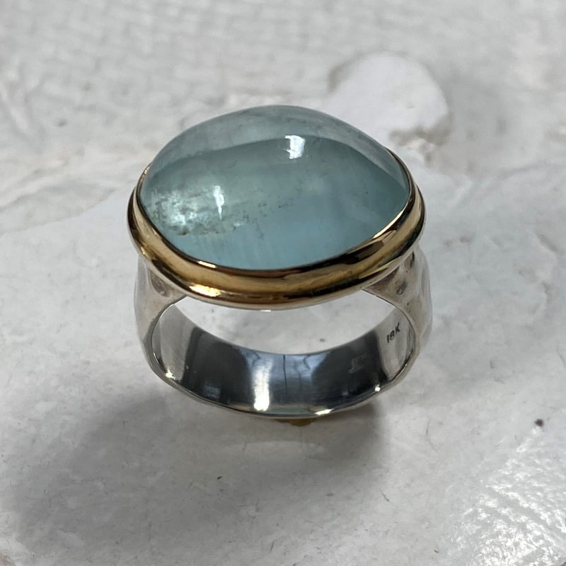 Sterling Silver ring with a Aquamarine in the center set in a bezel of 18 Karat Yellow Gold.