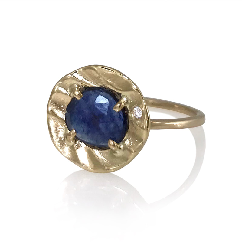 14 Karat Yellow Gold ring with a Blue Sapphire in the center and a frame of textured gold around it.