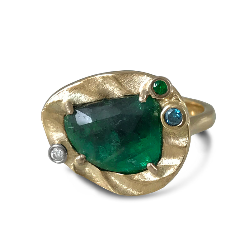 14 Karat Yellow Gold ring with an organic shaped Emerald in the center and three small stones on the bezel.