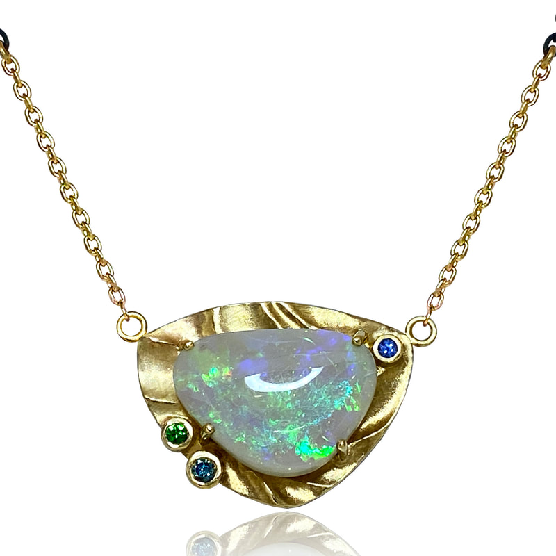 14 Karat Yellow gold pendant with a large opal in the center with a frame of textured Gold around it and accent stones.