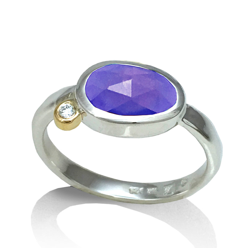 Sterling Silver ring with a bezel set oval Amethyst with a 14 Karat Yellow Gold bezel set diamond offset on the side of the Amethyst.