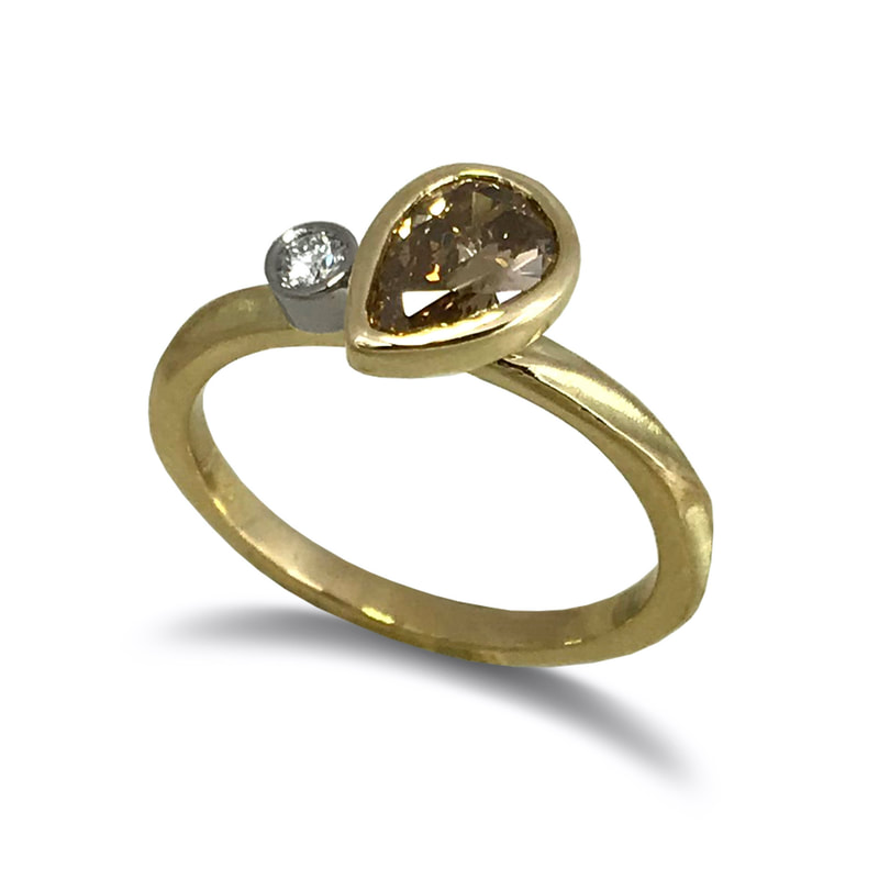 18 Karat Yellow Gold ring with a pear shaped Fancy Brown Diamond on an angle and a small diamond on one side.