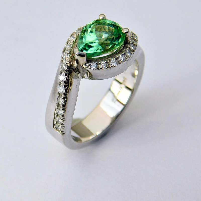 14 Karat White Gold ring with a pear shaped Green Tourmaline in the center and diamonds surrounding it that extend down each side of the band.