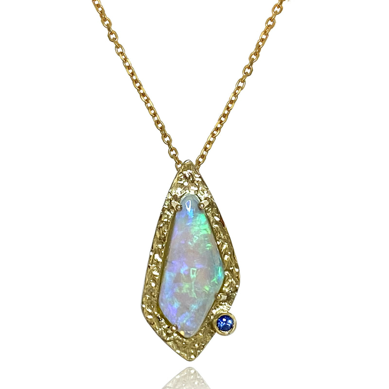 14 Karat Yellow gold pendant with an elongated opal in the center with a frame of textured Gold around it and a small Blue Sapphire.